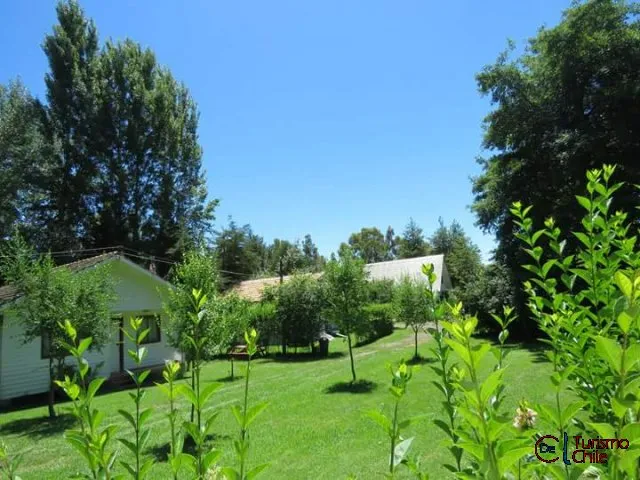 Vista de los jardines verdes con cabaña blanca al fondo en Jardín Salto del Laja