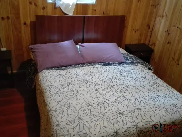 Dormitorio matrimonial con cama doble y paredes de madera en cabaña Jardín Salto del Laja