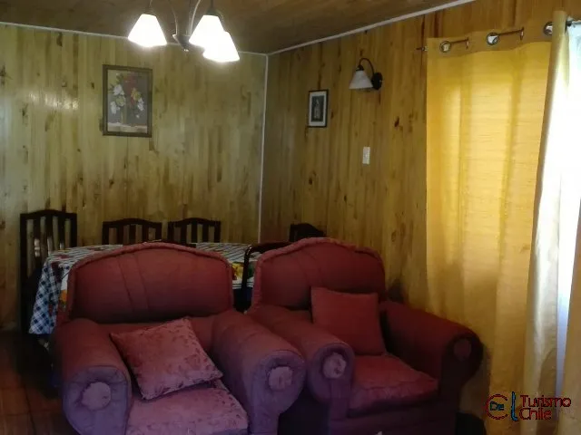 Living con sofás rosa y comedor en cabaña de madera de Jardín Salto del Laja